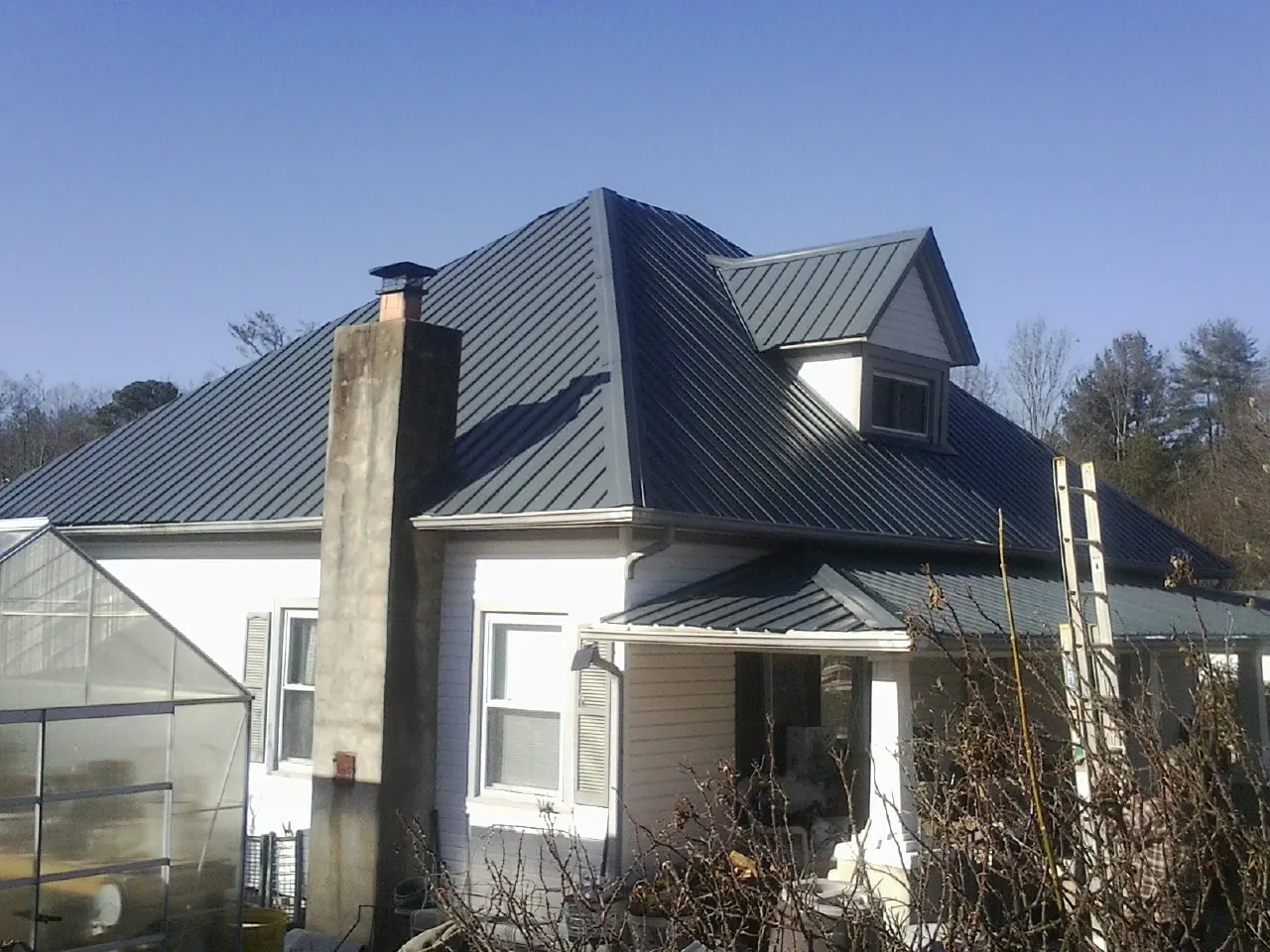 Dark blue standing seam metal roof on a white farmhouse with dormer — Slate & Tile Roof Repair by Roofing Brothers in Italy
