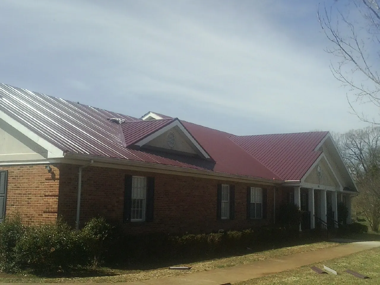 Red metal roof with gabled entries on a long brick building, from a Hail Damage Roof Repair job in Italy