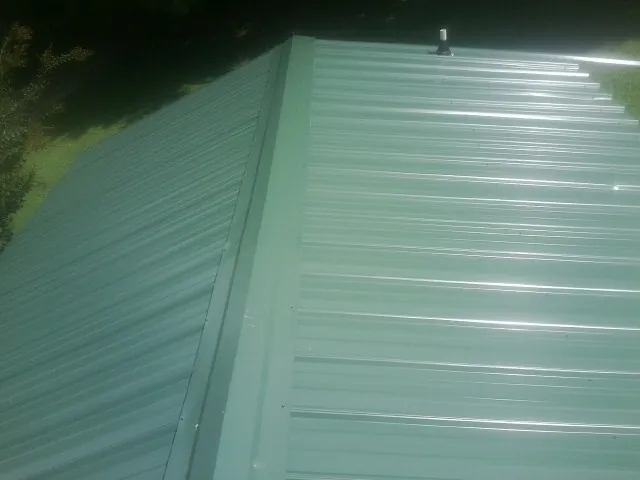 New green metal panels meeting at the ridge of a roof — Flat Roof Repair work by our crew in Italy
