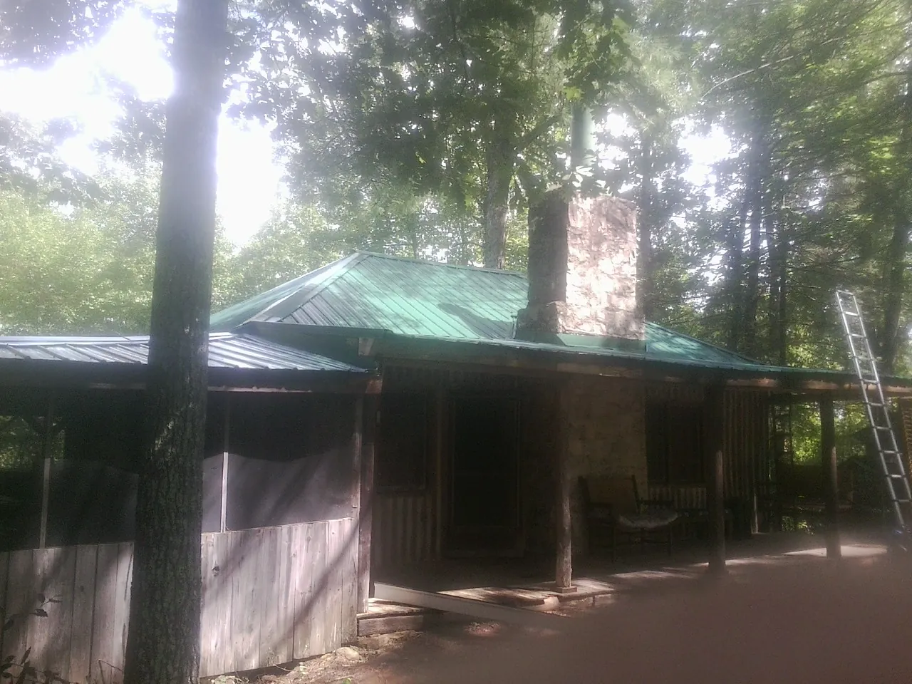 Green metal roof and stone chimney above a log cabin porch in Italy