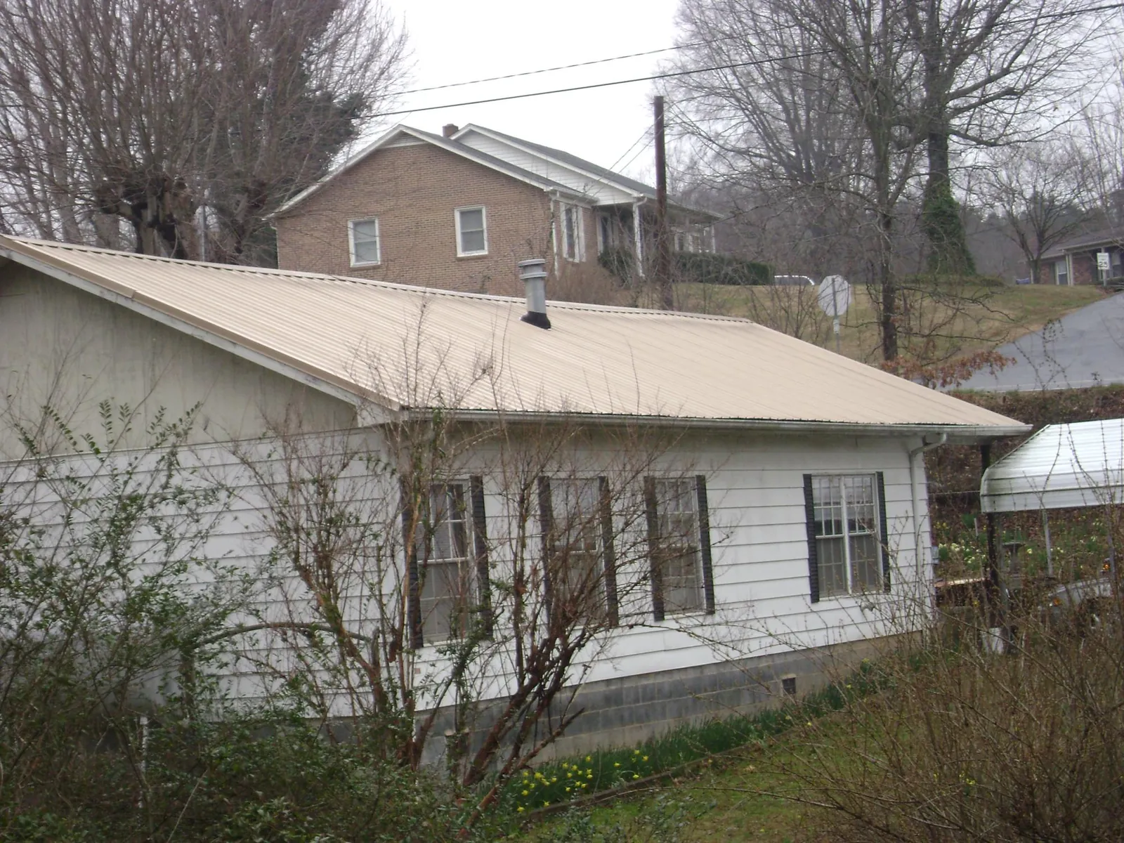 Tan metal roof on a white sided house set into a hillside — Commercial Roofing by Roofing Brothers in Italy