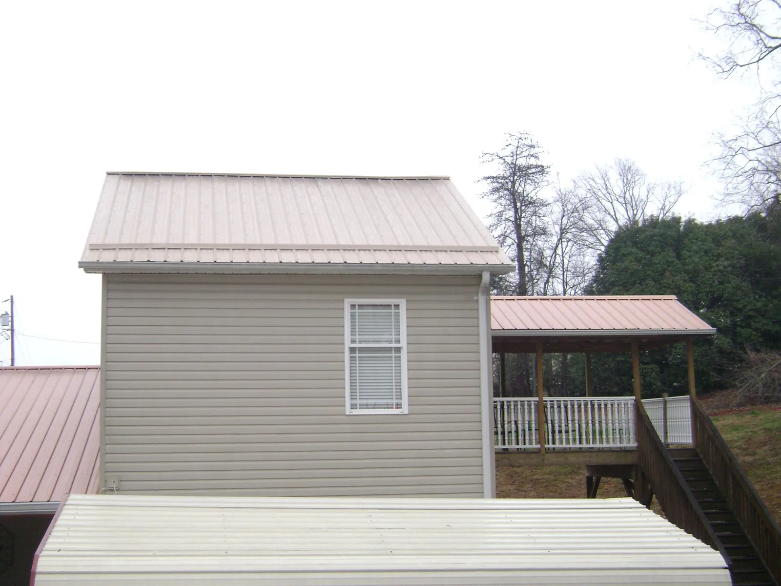 Tan metal roofs on a two story addition and attached porch, from a Roof Replacement job in Italy